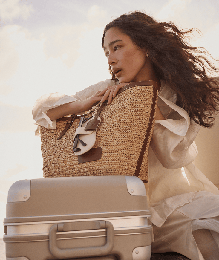 a woman in a white dress holding a straw bag and a suitcase
