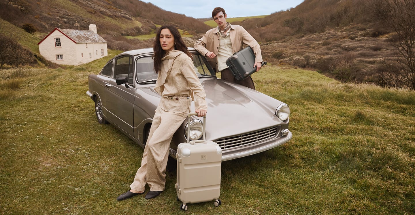 a man and woman with luggage standing next to a car