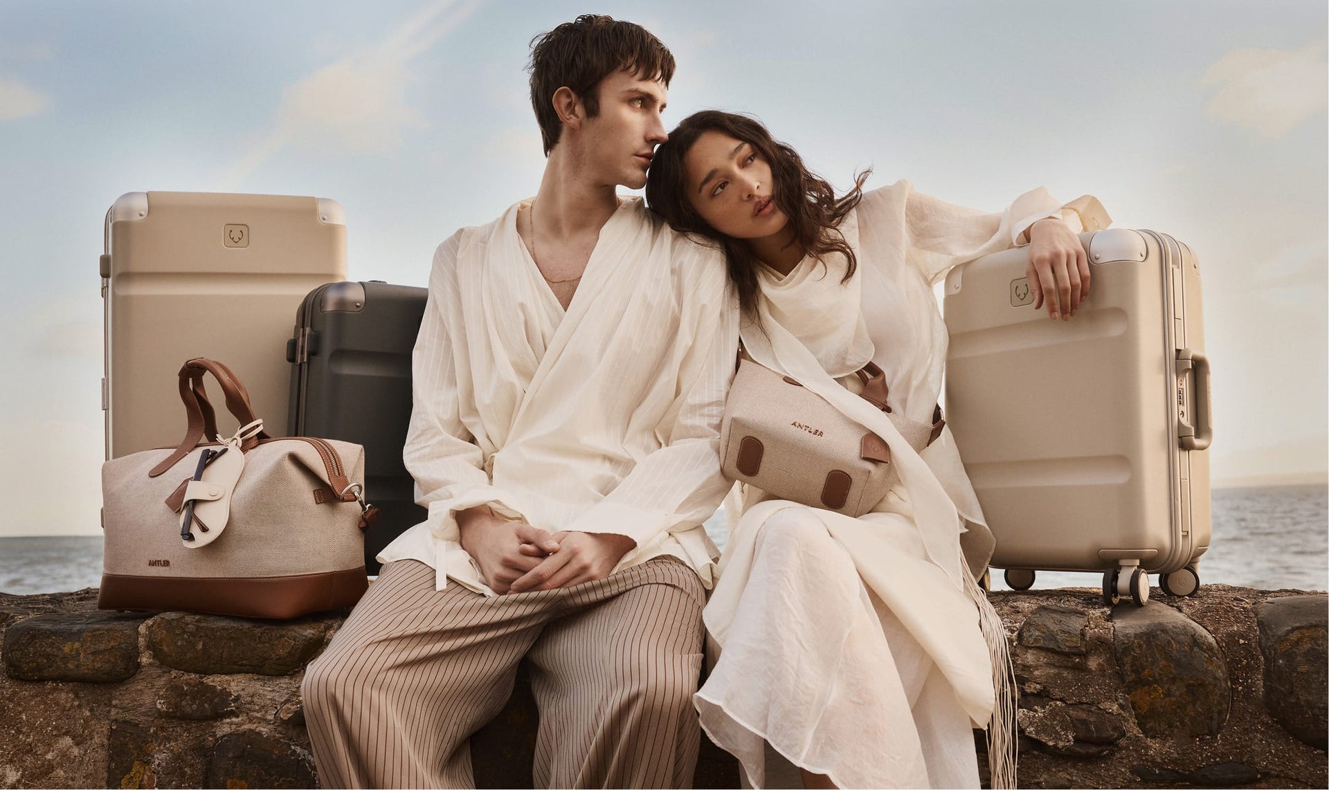 a man and woman sitting on a rock ledge with luggage