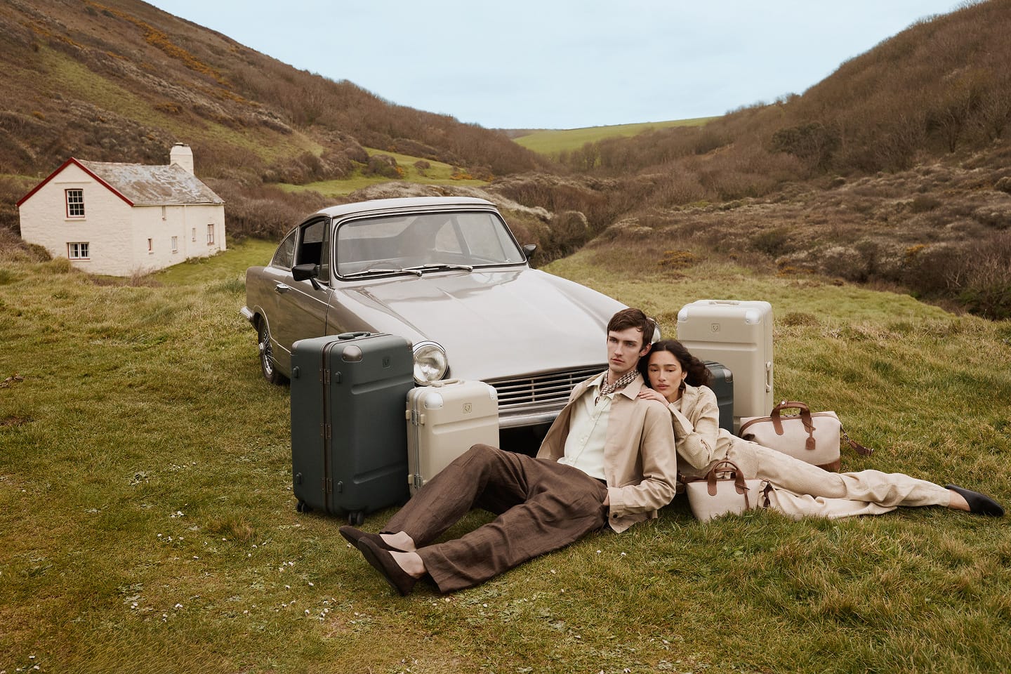 a man and woman sitting on grass with luggage