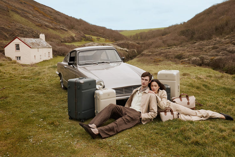 a man and woman sitting on grass with luggage