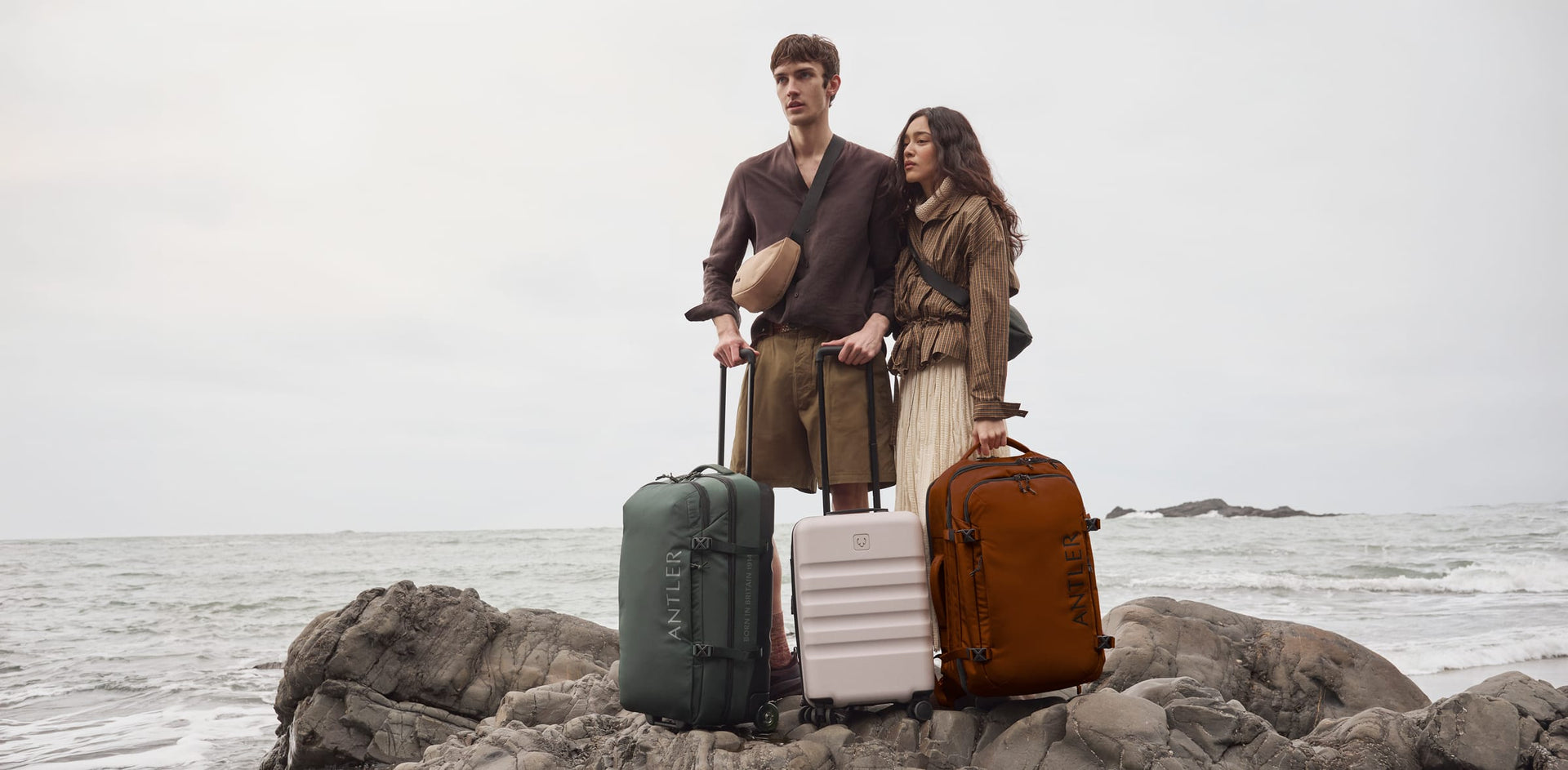 a man and woman standing on rocks with luggage