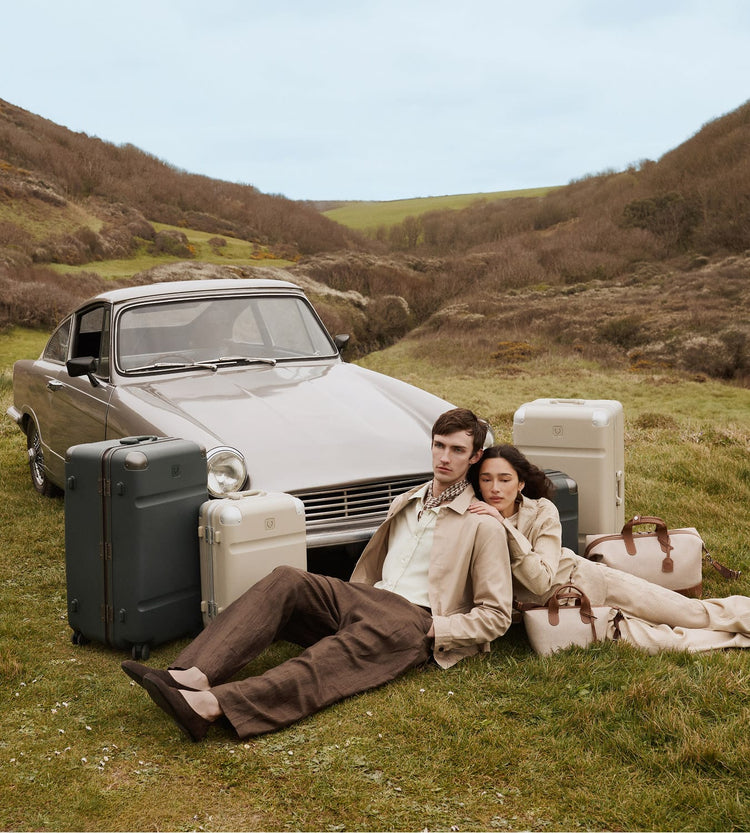 a man and woman sitting on the grass with luggage