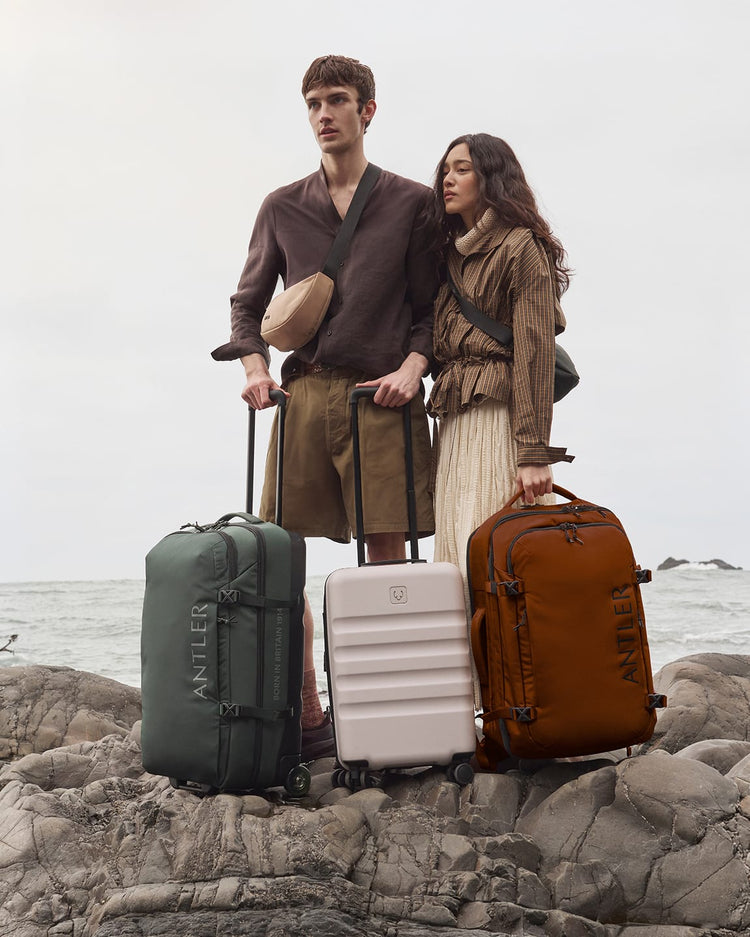 a man and woman standing with luggage on a rocky beach