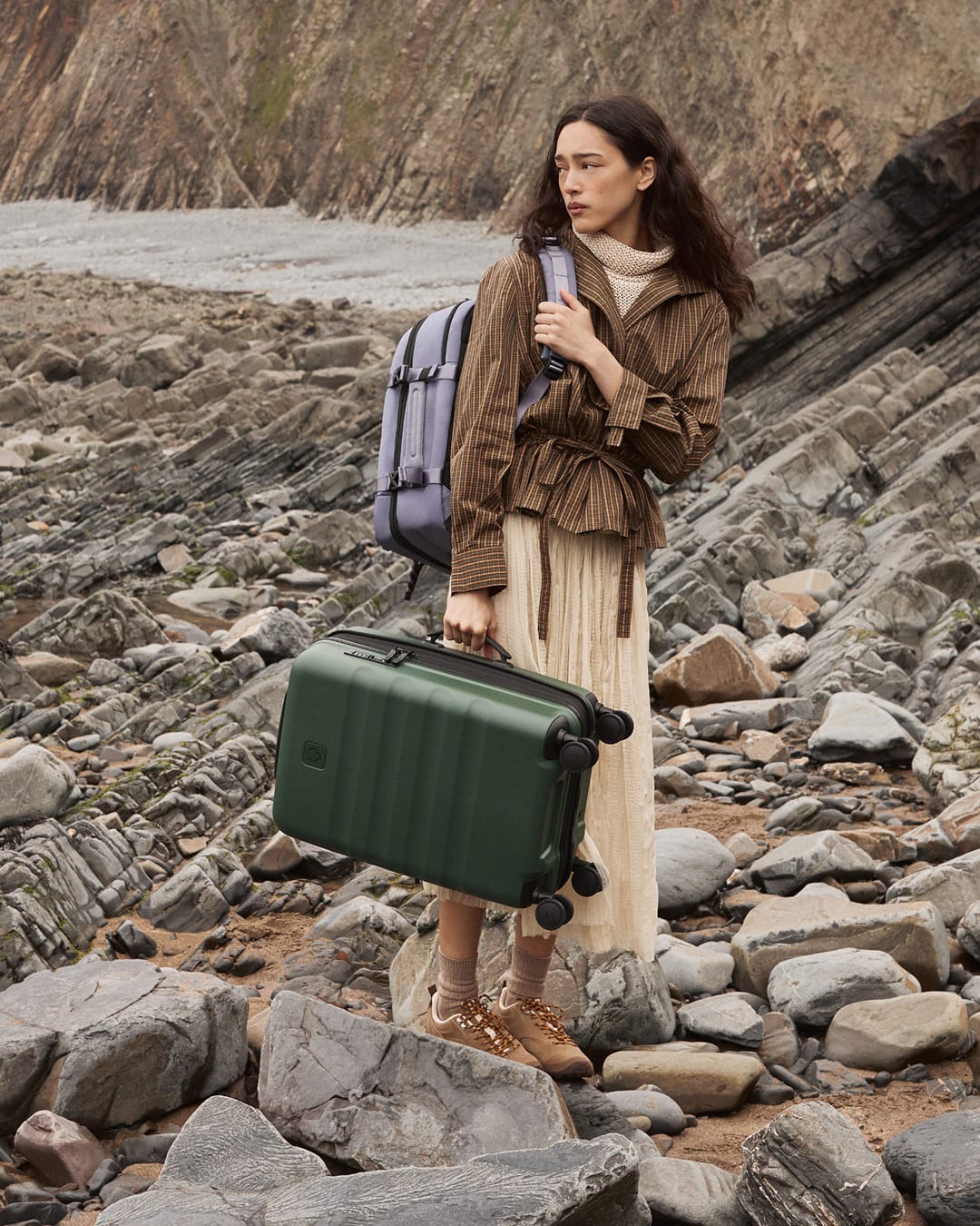 a woman holding a suitcase on a rocky beach