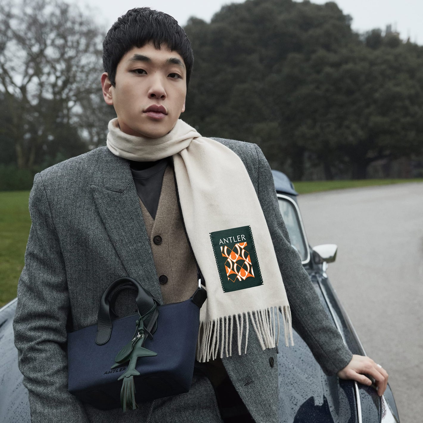 a man in a coat and scarf leaning on a car