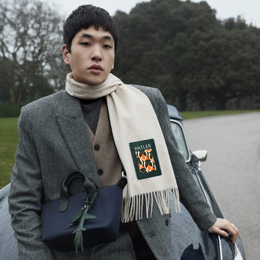 a man in a coat and scarf leaning on a car