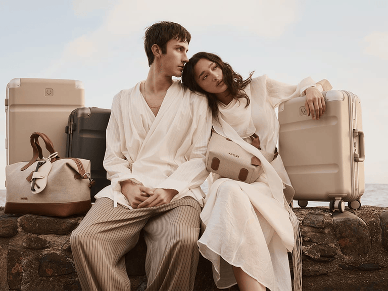 a man and woman sitting on a rock with luggage